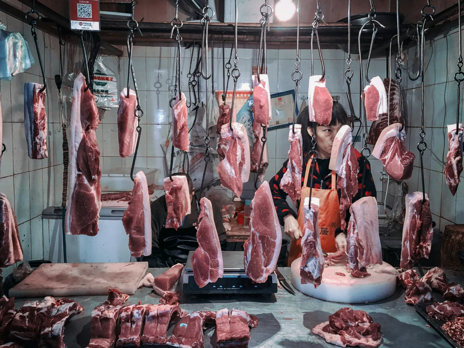 Butcher cutting meat beside hanging cuts in a processing room
